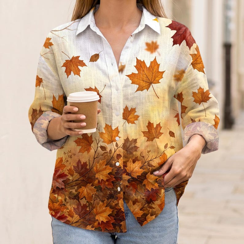 May include: A long-sleeved button-down shirt featuring a white base that transitions into a gradient of orange, yellow, and brown maple leaf patterns. The shirt has a classic collar, a front button placket, and cuffs rolled up to the mid-forearm.