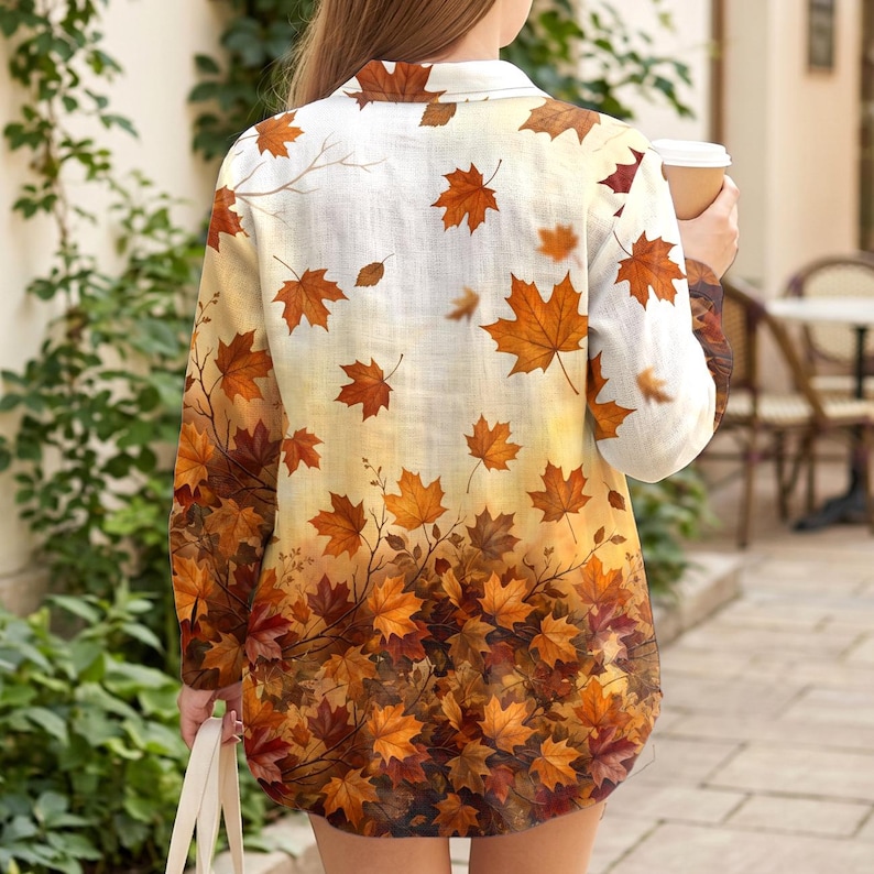 May include: A long-sleeved button-down shirt featuring an all-over print of autumn maple leaves in shades of orange, red, and brown. The pattern transitions from sparse leaves at the top to a dense, layered cluster of foliage at the hemline.