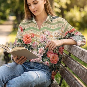 Puede incluir: Una camisa de manga larga con botones que presenta un estampado floral de rosas rosas, melocotón y blancas sobre un fondo de rayas chevron horizontales verdes y beige, combinada con pantalones vaqueros de color azul claro.