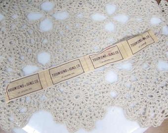 Op de afbeelding: Een strook vintage stoffen labels met de tekst "TOWNSEND & WALL CO. ST. JOSEPH, MO" in zwart gedrukt. De labels zijn beige en liggen op een crèmekleurig gehaakt kleedje.