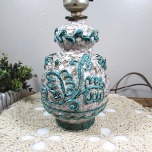 May include: A ceramic table lamp with a textured, speckled surface in shades of brown and white. The lamp features turquoise floral designs and a brass-colored neck. The lamp is approximately 12 inches tall.