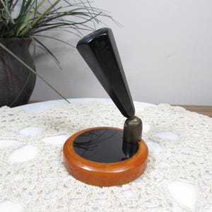 May include: A vintage pen holder with a black, angled pen rest and a round base. The base is made of a light brown material with a black center. The pen holder is a classic desk accessory.