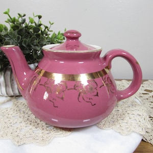 May include: A pink teapot with a gold trim and floral design. The teapot has a white interior and a lid.