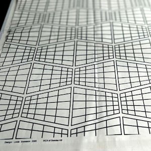 Op de afbeelding: Een close-up van een witte stof met een zwart geometrisch rasterpatroon. Het ontwerp toont een reeks onderling verbonden, onregelmatige vierhoeken. De tekst "Design: Linda Svensson 2005 IKEA of Sweden AB" is zichtbaar.