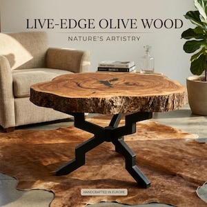 Puede incluir: Mesa de centro de madera de olivo con bordes naturales y forma orgánica. La tapa es de color marrón intenso con patrones de vetas únicos, soportada por una base de metal negro. La mesa está sobre una alfombra marrón, con un sillón beige al fondo.