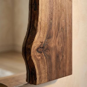 May include: A rectangular wooden mirror with a natural, live edge. The wood is a rich brown colour with visible grain and knots. The mirror is mounted on a wall, reflecting the surrounding environment.