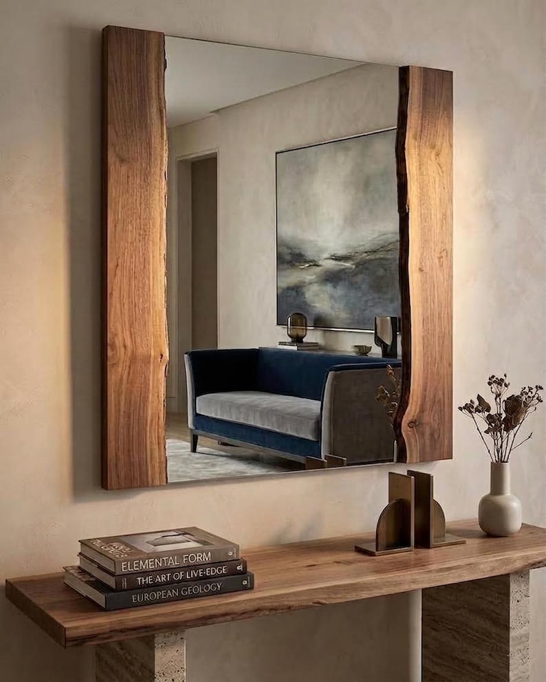 May include: A rectangular mirror with a natural wood frame. The frame has a live edge design. The mirror reflects a room with a blue sofa, artwork, and a wooden console table. Books and decorative items are on the table.