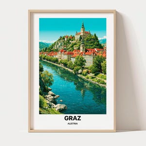 May include: A framed vertical art print featuring a vibrant landscape of Graz, Austria. The scene depicts a blue river flowing past buildings with red roofs and a prominent hilltop castle under a clear sky. The text GRAZ AUSTRIA is printed below.