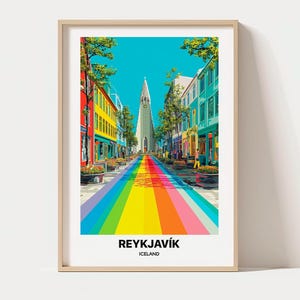 May include: A framed art print featuring a vibrant street scene in Reykjavík, Iceland. The image displays a rainbow-coloured path leading towards a tall, light-coloured church tower, flanked by colourful buildings under a bright blue sky.