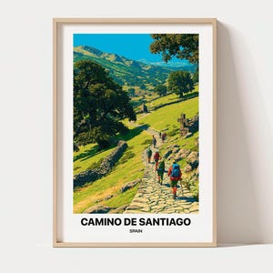 May include: A framed vertical art print featuring a landscape illustration of hikers on a stone path along the Camino de Santiago in Spain. The scene depicts green hills, large trees, and a stone cross. The text reads CAMINO DE SANTIAGO SPAIN.
