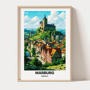Op de afbeelding: Een ingelijste verticale kunstdruk van de stad Marburg, Duitsland. De scène toont een groot kasteel op een heuvel boven een stad met oranje daken, vakwerkhuizen, groene bomen en een blauwe lucht. De tekst luidt MARBURG GERMANY.