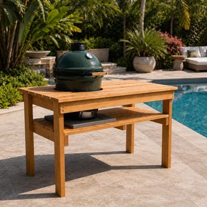 May include: A rectangular wooden grill table with a light brown finish, featuring a lower shelf and a circular cutout in the top surface. A dark green ceramic kamado-style grill with a silver temperature gauge is set into the table top.