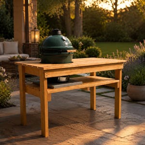 May include: A dark green ceramic kamado-style grill with a dome lid and a silver temperature gauge, integrated into a rectangular light-colored wooden table featuring a lower shelf and four sturdy legs for outdoor cooking and preparation.