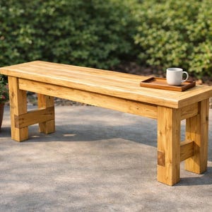 May include: A rectangular wooden bench with a natural light brown finish and sturdy block legs. A small wooden tray holding a white ceramic mug sits on the right side of the bench seat. The bench features visible wood grain and joinery details.