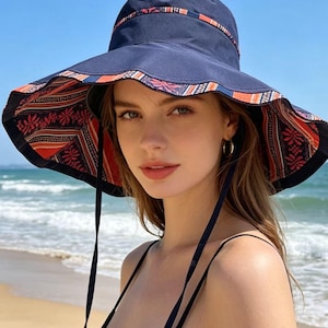 May include: Navy blue sun hat with a wide brim and patterned interior. The hat features a decorative band around the crown and long navy ties. The interior pattern includes red, orange, and white floral and geometric designs. A stylish accessory for sun protection.