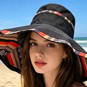 May include: A black sun hat with a wide brim, featuring a patterned band around the crown and a patterned underside. The hat's design incorporates red, orange, and white stripes and floral motifs. The hat is worn on a beach.