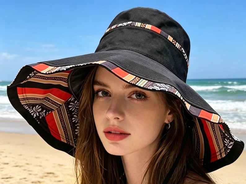 May include: A black sun hat with a wide brim, featuring a patterned band around the crown and a patterned underside. The hat's design incorporates red, orange, and white stripes and floral motifs. The hat is worn on a beach.