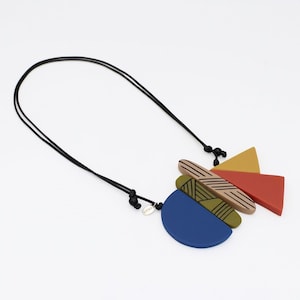 May include: A contemporary necklace with a black cord and a pendant of geometric shapes. The pendant features a blue semi-circle, red and yellow triangles, and a rectangular shape with linear patterns. The necklace has a silver tag.