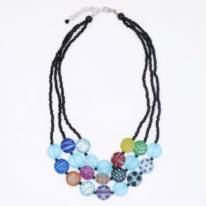 May include: A colorful necklace featuring three strands of small black beads. The necklace has a silver-tone clasp and is adorned with large, round, patterned beads in various colors, including blue, orange, and purple.