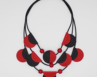 May include: A multi-layered necklace with black and red circular and semi-circular beads. The necklace is made of leather and has a black cord.