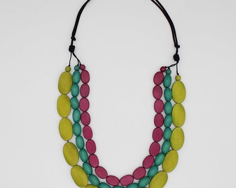 May include: A multi-strand necklace featuring three layers of oval-shaped wooden beads in lime green, teal, and magenta. The beads are strung on thin black cords that are knotted at the top to secure the strands together in a tiered arrangement.