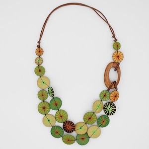 May include: A brown cord necklace with green and brown wooden circle pendants. The circles have a layered design with green, brown, and yellow accents.
