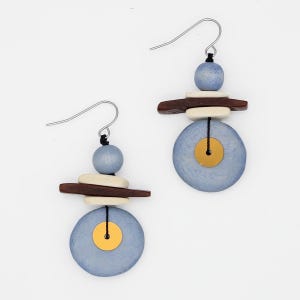 May include: A pair of handcrafted earrings with a unique, layered design. Each earring features a light blue disc with a gold-colored center, accented by stacked wooden and cream-colored elements. The earrings hang from silver-tone hooks.