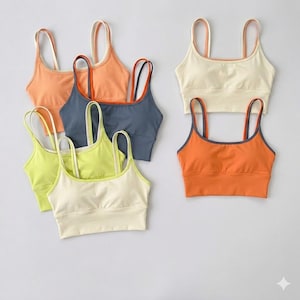 May include: A collection of colorful sports bras in various shades, including orange, yellow, and blue. Each bra features a scoop neck and thin straps, with contrasting trim details. The bras are designed for athletic activities.