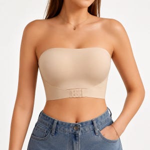 May include: A beige strapless bandeau top featuring a smooth, seamless construction with a front-facing hook-and-eye closure at the center. The garment is designed with a straight neckline and a fitted silhouette that sits above the waistline.