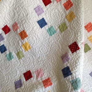 K&ouml;nnte beinhalten: Eine wei&szlig;e Steppdecke mit einem Rautenmuster aus bunten Stoffquadraten. Die Quadrate sind in verschiedenen Farben, darunter Rot, Orange, Gelb, Gr&uuml;n, Blau und Pink.