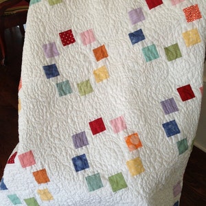 K&ouml;nnte beinhalten: Eine wei&szlig;e Steppdecke mit Patchwork-Muster, das bunte Quadrate in verschiedenen Rot-, Blau-, Gr&uuml;n-, Gelb- und Rosat&ouml;nen zeigt. Die Quadrate sind diagonal angeordnet.