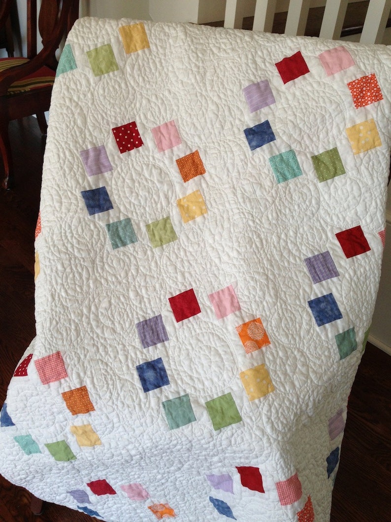 K&ouml;nnte beinhalten: Eine wei&szlig;e Steppdecke mit Patchwork-Muster, das bunte Quadrate in verschiedenen Rot-, Blau-, Gr&uuml;n-, Gelb- und Rosat&ouml;nen zeigt. Die Quadrate sind diagonal angeordnet.