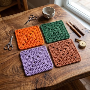 Puede incluir: Cuatro posavasos cuadrados de ganchillo de colores, naranja, verde, morado y marrón, sobre una mesa de madera. Herramientas de artesanía, como tijeras, ganchos de ganchillo y una cinta métrica, rodean los artículos hechos a mano, ideales para la decoración.