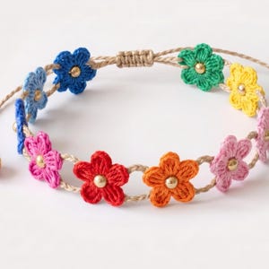 May include: A bracelet featuring a series of small, crocheted flowers in blue, pink, red, orange, green, and yellow. Each flower has a small gold-toned bead at its centre. The flowers are connected by a tan cord with an adjustable sliding knot closure.