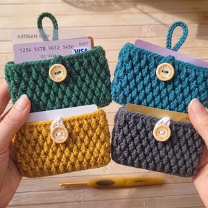 Peut inclure: Quatre porte-cartes crochetés à la main en vert, bleu sarcelle, jaune et gris. Chaque porte-cartes présente un point texturé, une fermeture à bouton en bois et une boucle pour un accès facile. Des cartes de crédit sont visibles.
