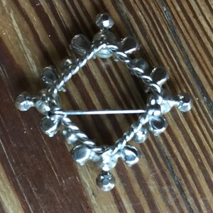 May include: A silver-toned metal brooch in a diamond shape, featuring a twisted wire frame adorned with small, round, clear faceted stones set at regular intervals along the perimeter and at each of the four points of the diamond structure.