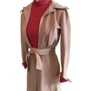 May include: A vintage-style coat in a tan and white checkered pattern, featuring a matching belt and red polka dot accents on the cuffs and collar. The coat is layered over a red polka dot turtleneck.