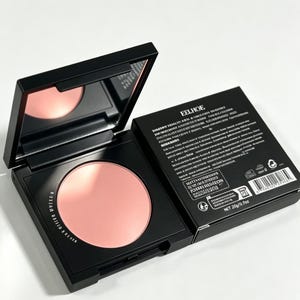 May include: A black square compact case containing a round light pink powder with an attached mirror in the lid, positioned next to its black cardboard box featuring the brand name EELHOE, white text, and a net weight of 0.7 ounces.