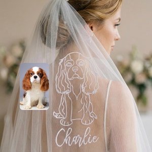 Könnte beinhalten: Ein durchsichtiger weißer Brautschleier mit einem individuell gestickten Cavalier King Charles Spaniel-Design und dem Namen "Charlie" in Schreibschrift. Ein kleines Foto des Hundes befindet sich in der Ecke. Der Schleier wird von einer Person mit blonden Haaren getragen.