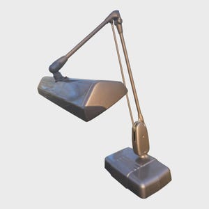 May include: A metallic gray desk lamp featuring an adjustable articulated arm and a rectangular head. The lamp has a rectangular base with a smooth finish and a long, slender neck that connects to the light housing, allowing for directional light.