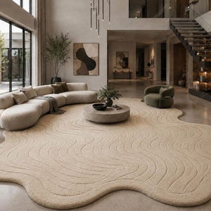 May include: A large, beige, irregularly shaped area rug with a textured, wavy, carved pattern across its surface. The rug features a soft, plush pile and organic, flowing edges that create a distinct, non-rectangular silhouette on the floor.