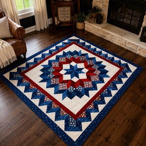 May include: A large, square quilt with a patriotic design. The quilt features a central starburst pattern in red, white, and blue, surrounded by a white background and a blue border. The quilt is placed on a dark wood floor.
