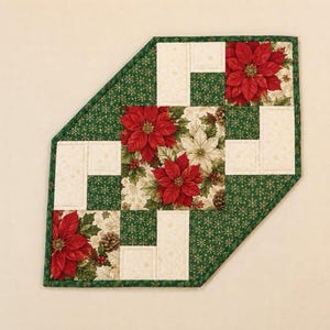 May include: A quilted table runner with a geometric pattern featuring red poinsettia flowers, green fabric with gold snowflake prints, and cream-colored fabric with subtle gold accents. The piece has a diagonal corner edge and green binding.