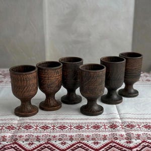 May include: A set of six dark brown, textured clay goblets with a rounded bowl, a short stem, and a circular base. Each goblet features a distinct wood-grain pattern on the exterior surface, showcasing a rustic, earthy appearance and uniform shape.