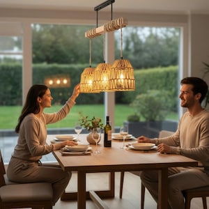 May include: A dining room scene featuring a wooden table set for a meal, illuminated by a three-light pendant lamp. The lamp has woven shades and a wooden beam. A couple is seated at the table, with a bottle of wine and glasses visible.
