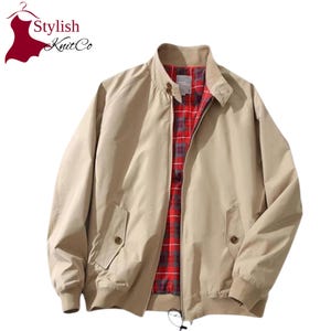 May include: A beige zip-up jacket featuring a stand-up collar with two buttons, long sleeves with ribbed cuffs, and two front pockets with button closures. The interior is lined with a red, grey, and black plaid fabric. The logo Stylish KnitCo is visible.