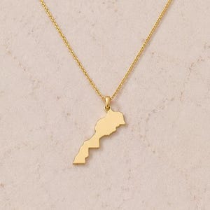 Peut inclure: Un collier doré avec un pendentif en forme de pays. Le pendentif est suspendu à une chaîne délicate. Le collier est présenté sur un fond neutre.