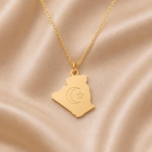 Peut inclure: Un collier doré avec un pendentif en forme de carte de l'Algérie. Le pendentif présente une surface lisse et polie avec un symbole de croissant de lune et d'étoile gravé au centre de la carte. Il est suspendu à une fine chaîne dorée.