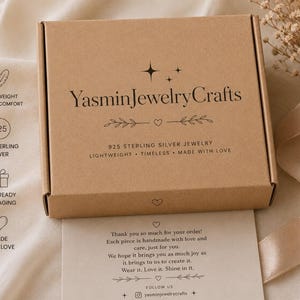 May include: A rectangular brown cardboard jewelry box with the text YasminJewelryCrafts printed in black on the lid. The box features decorative star and heart icons. Below the box is a thank you note with printed text and social media details.
