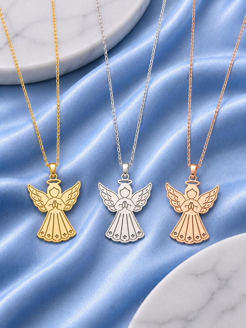 May include: Three necklaces featuring angel pendants in gold, silver, and rose gold tones. Each pendant depicts a stylized angel with wings spread, hands clasped in prayer, and a halo above the head, suspended from a matching delicate metal chain.